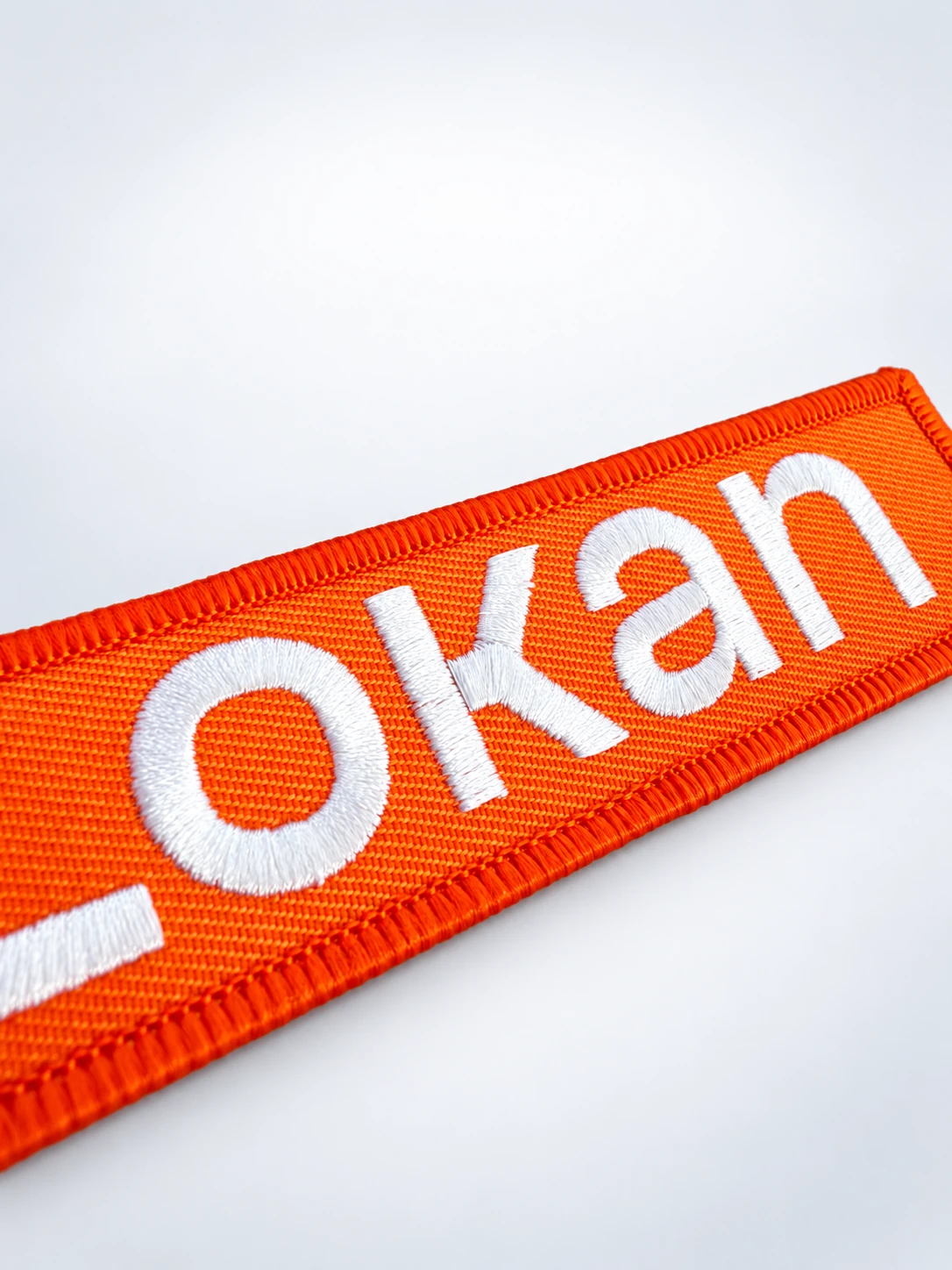 Gros plan en diagonale des fils blancs et de la bordure d’un porte-clés flamme orange Lokan, sur fond gris perle