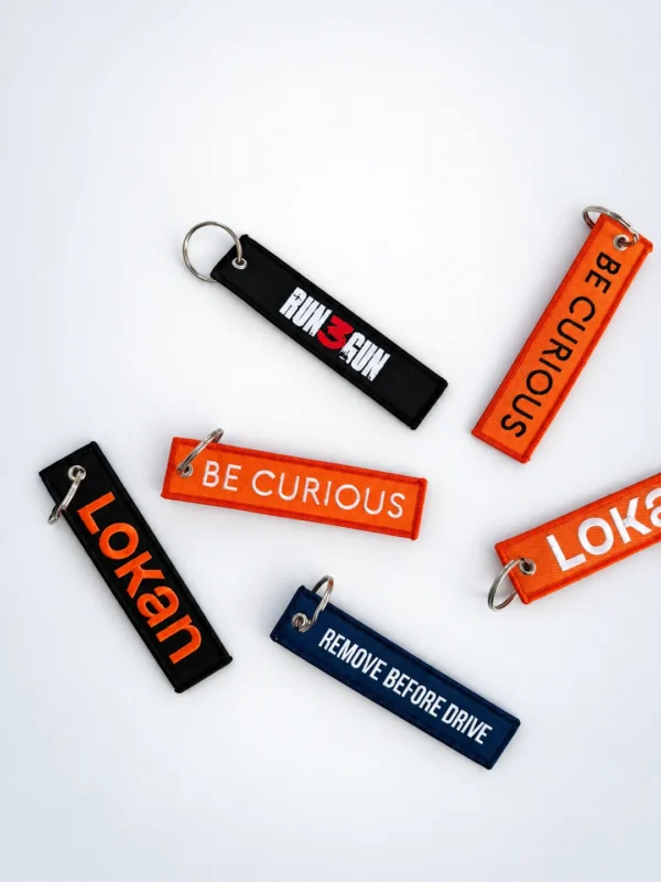 Exemples de porte-clés flamme personnalisés en tissé et brodé, modèles Run3gun, BE CURIOUS, Lokan et Remove before drive
